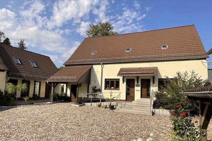 Ansicht eines Innenhofs mit mehreren Gebäuden und gepflastertem Boden, umgeben von Pflanzen und blauem Himmel.